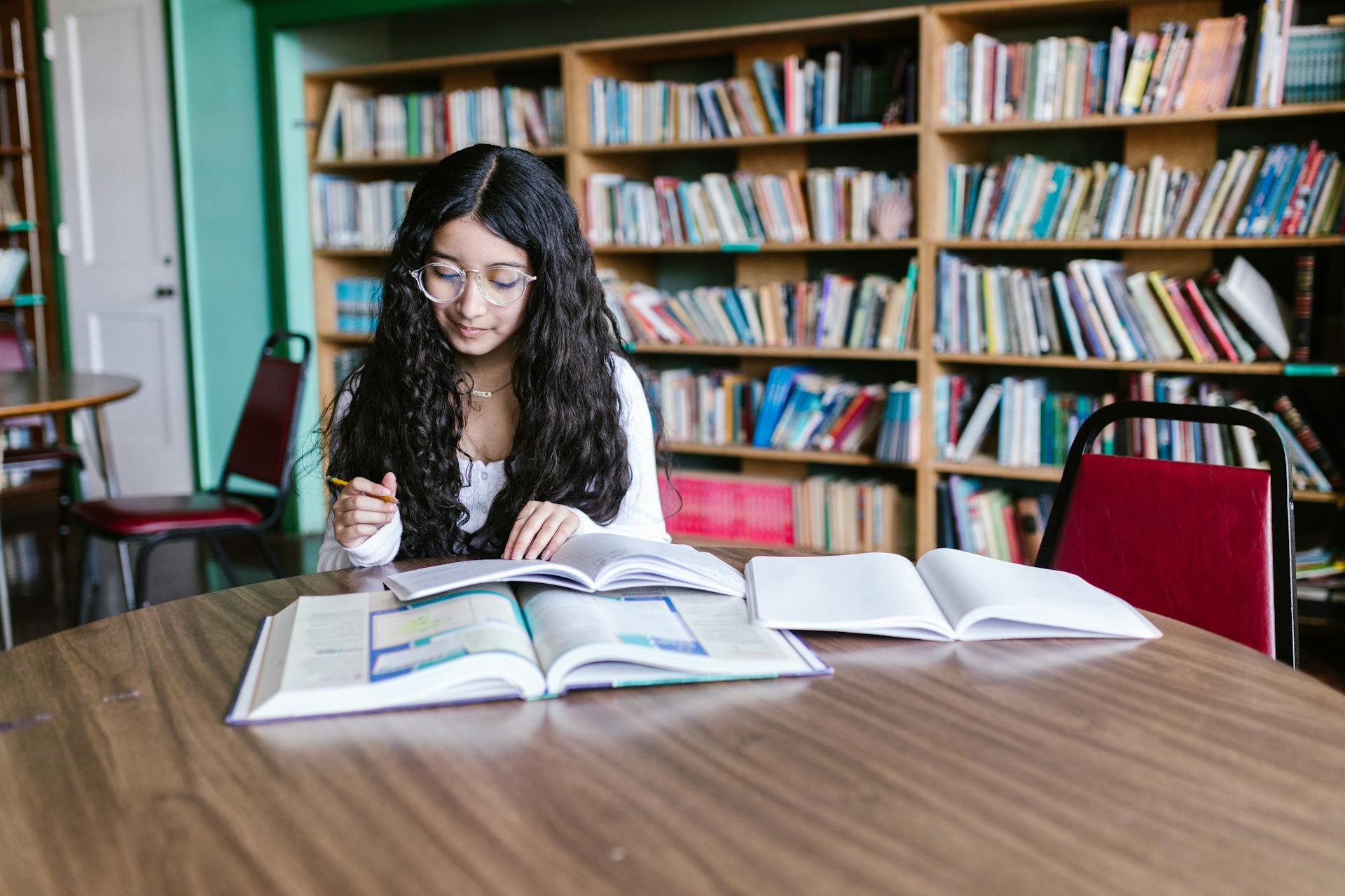 Grammar Exercise: A girl reading a book while sitting on a chair inside the library